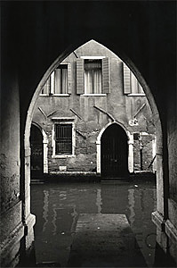 Black and white photo of the Calle de l'Aquila Nera which ends in an arch near Rialto reflecting the essential vernacular design of Venice, Italy